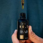 close up view of a person's hand holding a small black bottle of CBD oil and a dropper over it