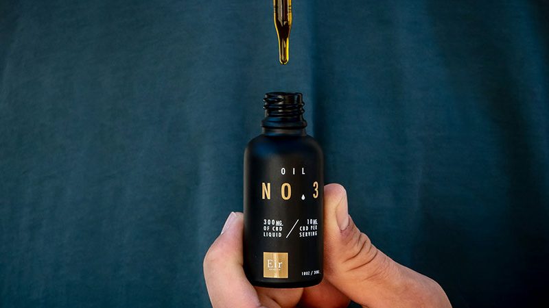 close up view of a person's hand holding a small black bottle of CBD oil and a dropper over it